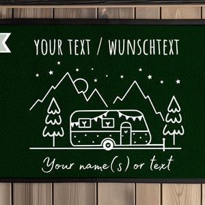 Puede incluir: Felpudo verde oscuro con borde negro. La alfombra presenta un dibujo lineal blanco de una caravana, monta&ntilde;as, &aacute;rboles, estrellas y el texto "YOUR TEXT / WUNSCHTEXT" y "Your name(s) or text".