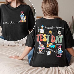 May include: Black t-shirt featuring Minnie Mouse with a pencil and the name "Emily". The back of the shirt has the words "TEST DAY" with various Disney characters and phrases like "You got this" and "Smash the test".