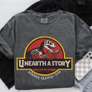 Unearth a Story Dinosaur Shirt, Summer Reading 2026 Shirt, Teacher Reading Shirt, Librarian Gift, Prehistoric Summer Reading Shirt