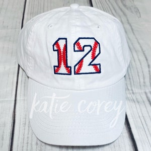 May include: White baseball cap with the number 12 embroidered in red and blue on the front. The number is styled to look like a baseball.