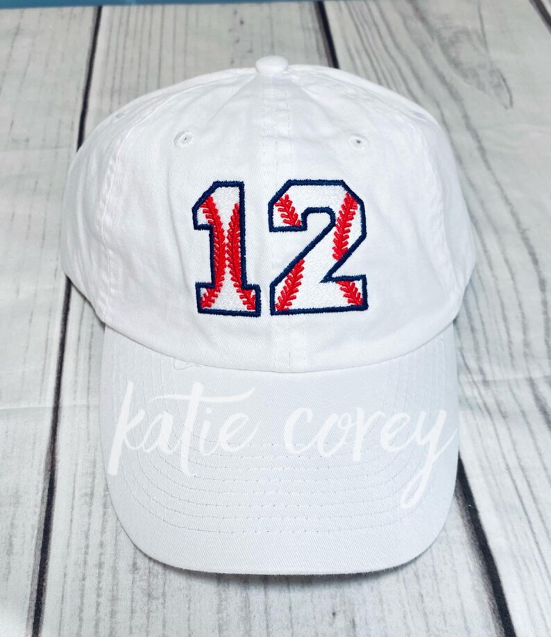 May include: White baseball cap with the number 12 embroidered in red and blue on the front. The number is styled to look like a baseball.