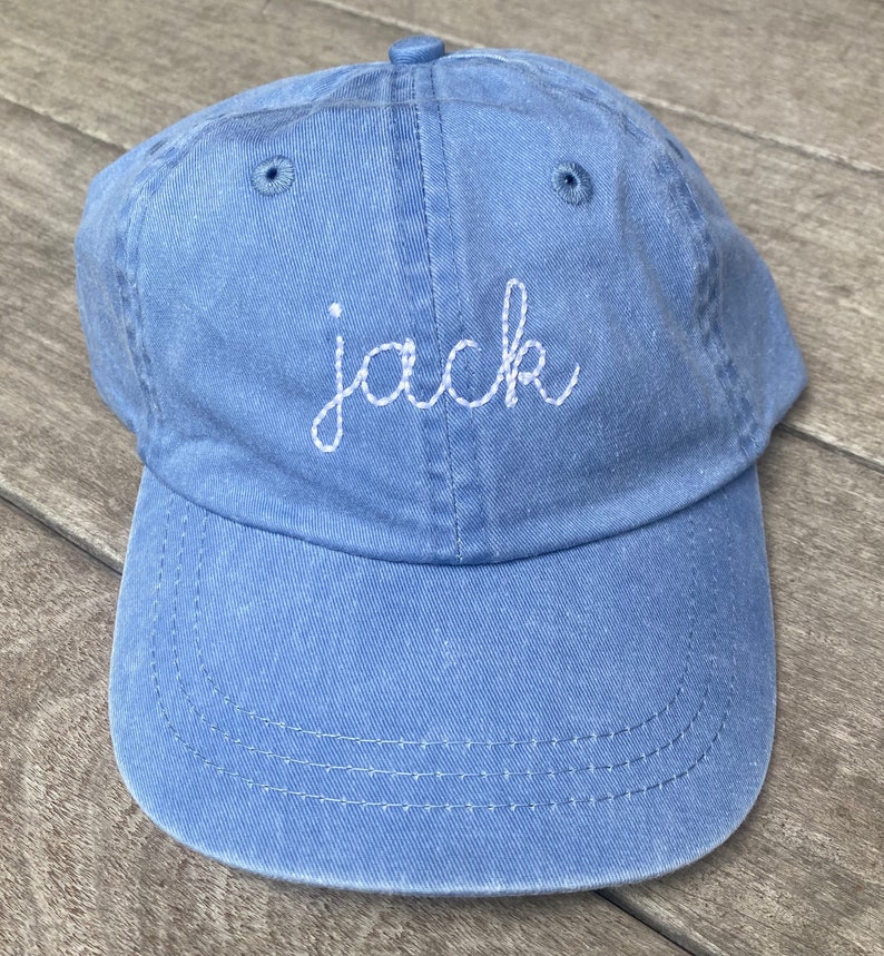 Puede incluir: Una gorra de b&eacute;isbol de denim azul con costuras blancas. La palabra "jack" est&aacute; bordada en la parte delantera de la gorra con hilo blanco.