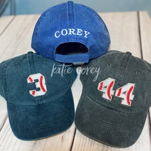 May include: Three baseball caps, one blue with the name "COREY" embroidered on the back, and two dark green with baseball numbers "3" and "44" embroidered on the front.