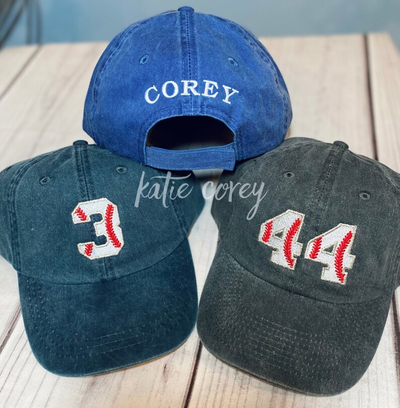 May include: Three baseball caps, one blue with the name "COREY" embroidered on the back, and two dark green with baseball numbers "3" and "44" embroidered on the front.