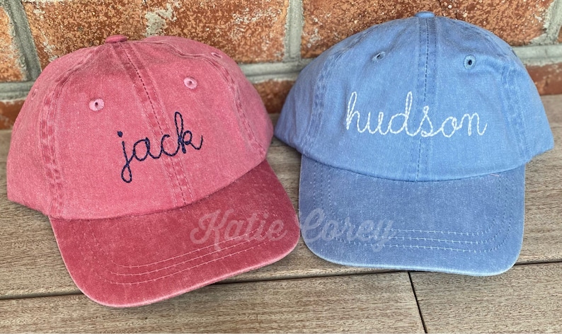 Puede incluir: Dos gorras de b&eacute;isbol personalizadas, una roja con el nombre "jack" bordado en azul marino, y otra azul con el nombre "hudson" bordado en blanco.