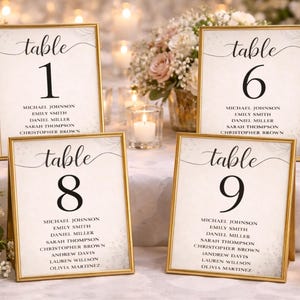 Puede incluir: Cuatro carteles con números de mesa enmarcados con marcos dorados. Cada cartel muestra un número de mesa en letras negras grandes, con los nombres de los invitados debajo. Los carteles están colocados sobre una mesa con velas y arreglos florales.