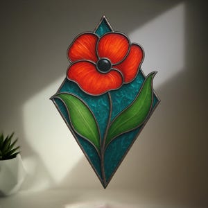 May include: A stained glass poppy flower with a vibrant red bloom and a black center. The flower is set against a teal background within a diamond-shaped frame, with green leaves and a dark border. A decorative piece.
