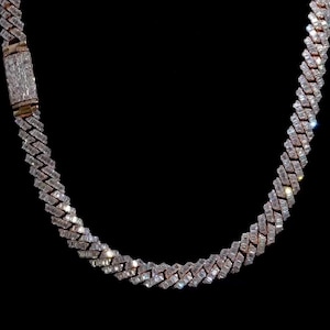 Könnte beinhalten: Eine funkelnde Halskette mit Diamanten vor schwarzem Hintergrund. Die Kette besteht aus rechteckig geschliffenen Steinen, die in einem sich wiederholenden Muster angeordnet sind und einen funkelnden Effekt erzeugen. Der Verschluss ist ebenfalls mit Diamanten besetzt.