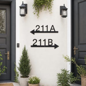 May include: Two black metal address signs mounted on a light-colored wall between two dark doors. The top sign displays 211A with an arrow pointing left, and the bottom sign displays 211B with an arrow pointing right. Both signs are horizontal.