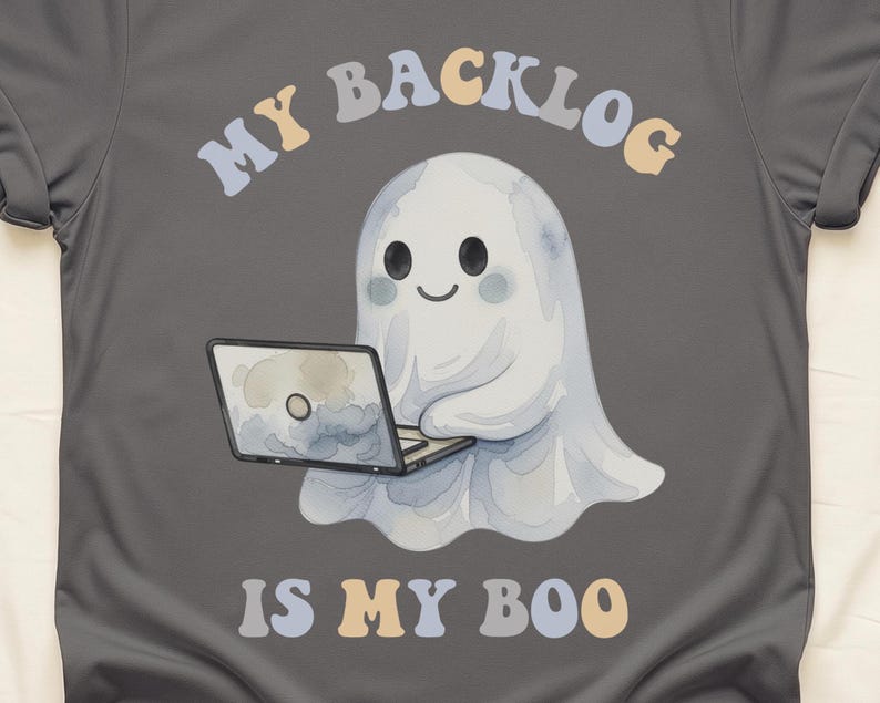 May include: A charcoal grey t-shirt featuring a graphic of a white ghost using a laptop. Above the ghost, the text reads MY BACKLOG in a curved, multi-coloured font. Below the ghost, the text reads IS MY BOO in the same multi-coloured font.