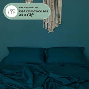 May include: A solid dark teal bedding set featuring two matching pillowcases and a flat sheet. A light green graphic overlay at the top displays the text: BUY A BEDDING SET Get 2 Pillowcases as a Gift, accompanied by an icon of two pillows.