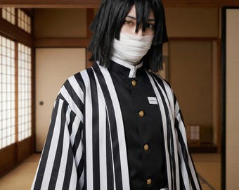 Puede incluir: Un haori de rayas blancas y negras sobre una chaqueta de uniforme negra con botones dorados. El conjunto incluye un cinturón blanco con hebilla plateada y un vendaje blanco envuelto alrededor de la parte inferior del rostro. Pelo negro y a capas.