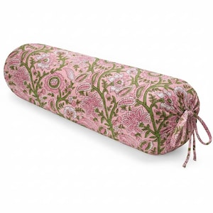 Puede incluir: Un cojín cilíndrico con un estampado floral rosa. El diseño presenta flores rosas, detalles blancos y vides verdes sobre un fondo rosa claro. La almohada está atada en un extremo con lazos de tela a juego.