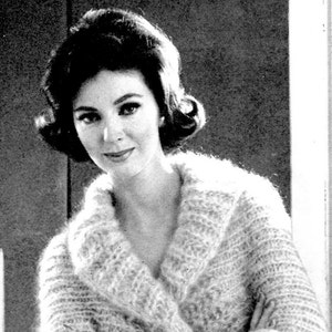 May include: A woman with dark hair styled in a bouffant and a white knitted cardigan with a shawl collar.
