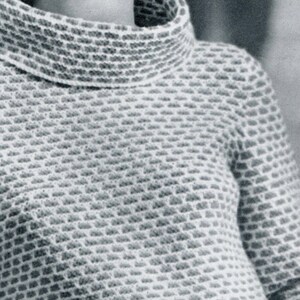 K&ouml;nnte beinhalten: Nahaufnahme einer Frau, die einen wei&szlig;en Pullover mit strukturiertem Muster tr&auml;gt. Der Pullover hat einen hohen Kragen und lange &Auml;rmel. Die Frau tr&auml;gt einen silbernen Ohrring am linken Ohr.