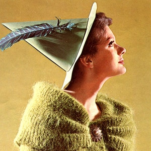 May include: A woman wearing a green knitted sweater with a large, green, pointed hat with a feather. The hat has a white brim. She is looking up and to the right.