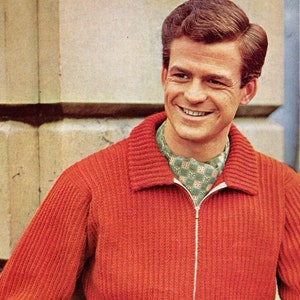 Op de afbeelding: Een man draagt een rode gebreide trui met een rits en een groen-witte gestreepte sjaal.