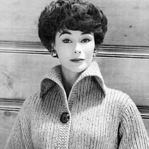 May include: A woman with short, dark hair wearing a light gray knitted cardigan with a large collar and a single button.