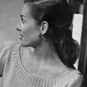 May include: A woman with her hair pulled back in a bun, wearing a light gray sweater with a scoop neck.