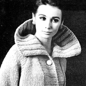 May include: A close-up of a woman wearing a knitted cardigan with a large collar. The cardigan is a light gray color and has a button closure.