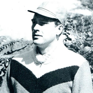 May include: A black and white photo of a man wearing a light gray sweater with a black V-shaped design and a light gray cap.