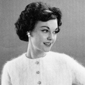 Puede incluir: Una mujer con el pelo oscuro peinado en un bouffant lleva un cárdigan blanco peludo con botones de perla.