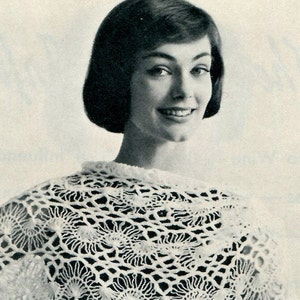 May include: A woman with short dark hair wears a white crocheted shawl with a lacy pattern.