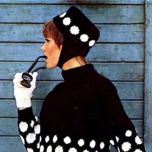 May include: A black and white knit sweater with a large white polka dot pattern. The sweater has a turtleneck and long sleeves. The model is wearing a black and white knit hat with a white pom-pom.