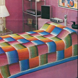 May include: A colorful knitted throw blanket with a checkered pattern in shades of pink, blue, green, orange, and white. The blanket is draped over a bed with a pink headboard.