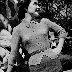 Peut inclure: Une femme portant un cardigan en tricot gris à col et fermeture boutonnée. Le cardigan a une taille cintrée et est ceinturé d'une ceinture en cuir marron. Elle se tient à côté d'une sculpture en pierre.