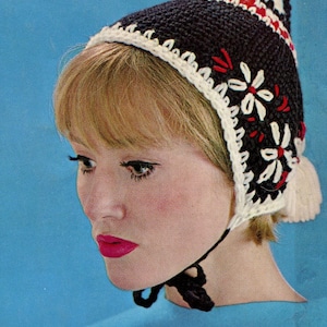May include: A woman wearing a black and white crocheted hat with red embroidery. The hat has a long tassel and a brim that covers her ears. She is wearing a blue shirt.