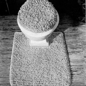 May include: A white toilet seat and toilet bowl rug with a fluffy, textured surface.