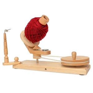 May include: A wooden yarn swift with a large ball of red yarn. The swift has a wooden base, a rotating wheel, and a spindle to hold the yarn. The yarn is a vibrant red color. The swift is designed for winding yarn.