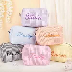 Puede incluir: Seis neceseres personalizados a rayas verticales en varios colores: morado, azul, naranja, negro, rosa y amarillo. Cada neceser tiene un nombre bordado en un color complementario. Cuentan con cierre de cremallera y pequeñas asas laterales.