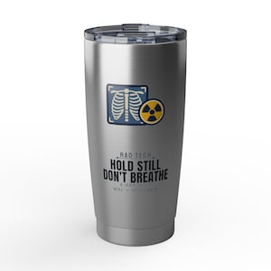 Puede incluir: Un vaso de acero inoxidable plateado con tapa de plástico transparente. El frente presenta un gráfico de una radiografía de caja torácica humana y un símbolo de radiación amarillo. Texto: RAD TECH, HOLD STILL DON'T BREATHE, X-RAY, CT, MRI, PORTABLE.