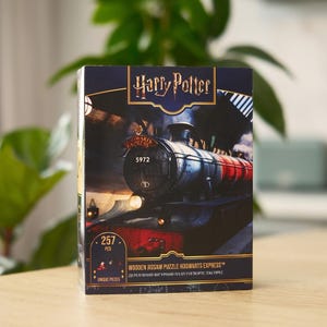 May include: A boxed wooden jigsaw puzzle featuring the Hogwarts Express train from the Harry Potter series. The box is dark blue with gold lettering and an image of the train. The puzzle contains 257 pieces.
