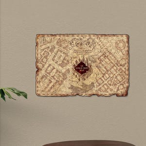May include: A rectangular wooden map with a distressed, aged appearance. The map features intricate details and text, including "Marauder's Map" in a central emblem. The map is mounted on a neutral-colored wall, with a wooden table below.