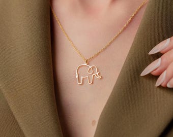 May include: A gold-colored elephant pendant necklace. The pendant is a simple outline of an elephant. The necklace is worn over a green blazer.