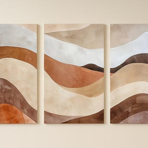 May include: Three-piece wall art with abstract landscape designs. Each panel shows layered, undulating shapes in shades of brown, beige, and white, creating a textured, earthy aesthetic. The artwork is mounted on a neutral-toned wall.