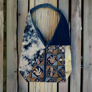 Puede incluir: Bolso tote hecho a mano con un diseño de patchwork. El bolso presenta un estampado tie-dye en blanco y azul marino, junto con cuadrados con motivos florales y de pájaros en tonos marrón, rosa y azul. La correa es azul marino.