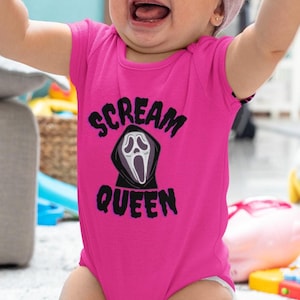 Puede incluir: Un beb&eacute; con un body rosa brillante con las palabras "SCREAM QUEEN" y un gr&aacute;fico de cara de fantasma. El beb&eacute; lleva una diadema lila clara y tiene los brazos en alto. Imagen tomada en interiores.