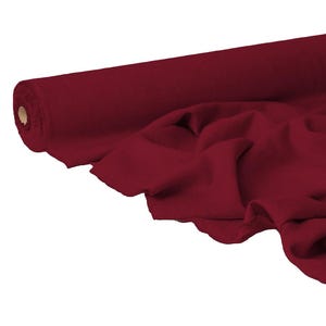 Puede incluir: Un rollo de tela rojo oscuro, parcialmente desenrollado para revelar pliegues suaves. La tela es de color liso, con un ligero brillo, y parece ser un material de peso medio. El rollo está posicionado en el lado izquierdo de la imagen.