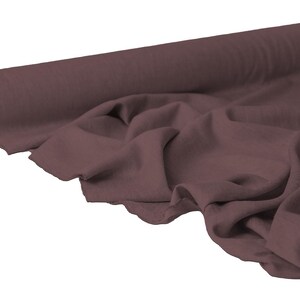 May include: A roll of dark mauve fabric with a soft, flowing drape. The fabric is partially unrolled, revealing the texture and folds of the material. The fabric appears to be a medium weight, suitable for various sewing projects.