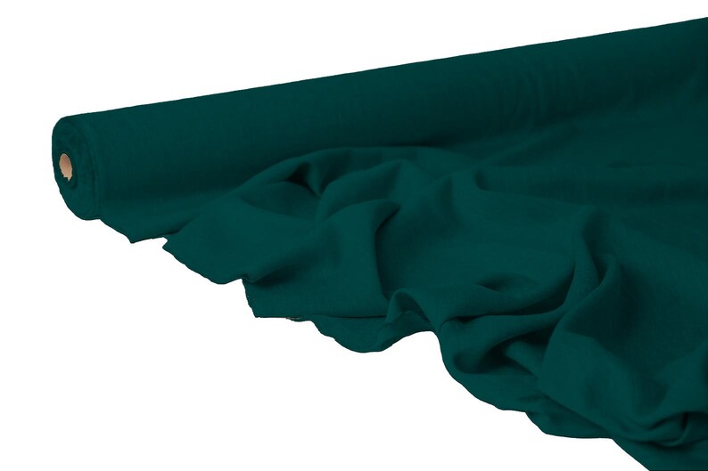 May include: A roll of teal fabric, partially unrolled to reveal the soft texture. The fabric is a solid, deep teal color, with visible folds and drapes. The roll's core is a light brown color.