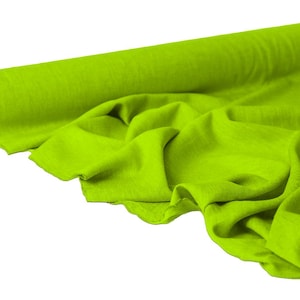 May include: A roll of bright green fabric, partially unrolled to reveal the textured material. The fabric is a vibrant, solid color, with visible folds and creases. The roll is on the left side of the image, with the fabric cascading down.