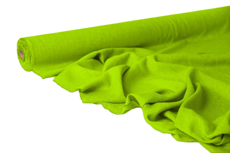 May include: A roll of bright green fabric, partially unrolled to reveal the textured material. The fabric is a vibrant, solid color, with visible folds and creases. The roll is on the left side of the image, with the fabric cascading down.
