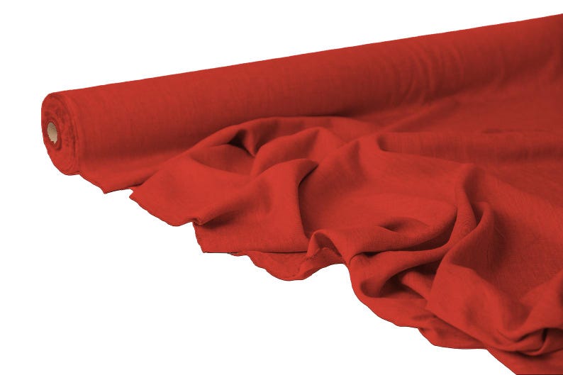 May include: A roll of vibrant red fabric, partially unrolled to reveal soft folds. The fabric is a solid color, with a smooth texture. The image is set against a white background, highlighting the rich color and texture of the material.