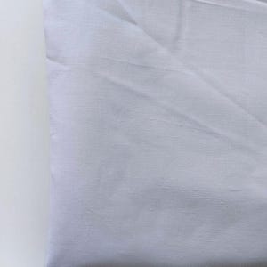 May include: A folded, light-colored fabric, possibly linen or cotton, with visible texture and subtle shadows. The fabric appears to be a solid, pale color, possibly white or a very light gray, and is neatly folded.