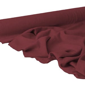 May include: A roll of burgundy fabric with a soft, draped appearance. The fabric is unrolled, revealing its texture and color. The material is likely used for sewing, crafting, or upholstery projects.