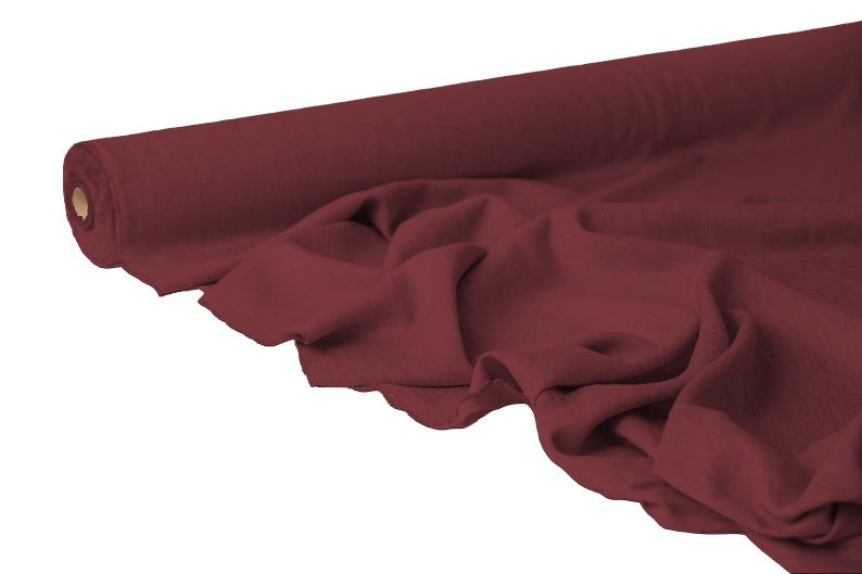 May include: A roll of burgundy fabric with a soft, draped appearance. The fabric is unrolled, revealing its texture and color. The material is likely used for sewing, crafting, or upholstery projects.